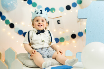 Fototapeta na wymiar Caucasian small infant baby boy celebrating his first birthday blonde child with blue crown and number one on it one year old happy kid