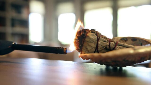 A lighter comes in to burn a wrapped bundle of sage herb to cleanse a home of negativity, bacteria and virus. 