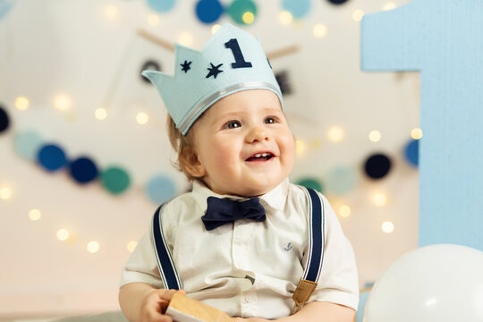 Caucasian small infant baby boy celebrating his first birthday blonde child with blue crown and number one on it one year old happy kid