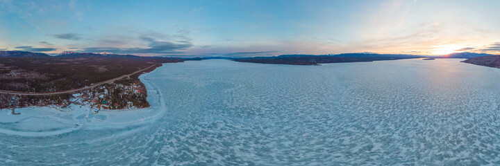 Drone, aerial view of a northern Canadian sunset with huge frozen lake and blue sky, partial clouds in distance. Taken along the Alaska Highway in spring time, April. 