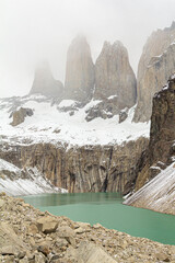 montanhas e pico das Torres Del Paine com lindo lago verde e pedras na lateral e céu enevoado 