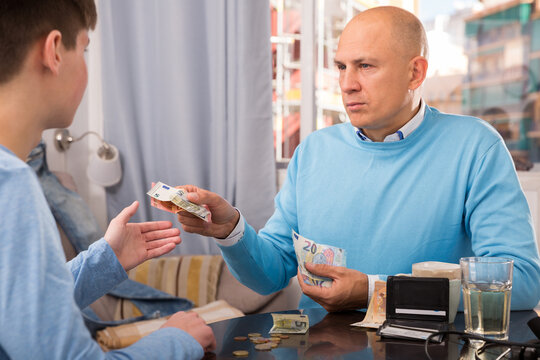 Portrait Of Positive Man Giving Money To Teen Boy In Home Interior