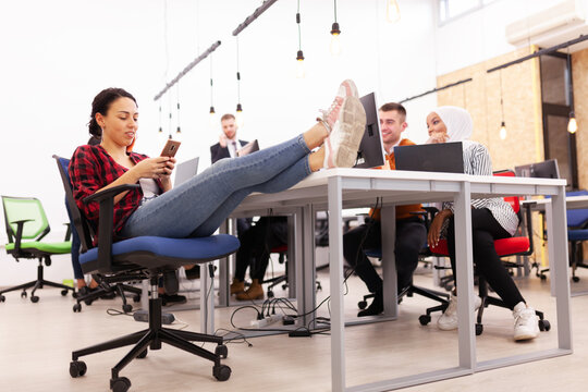 Group of multiethnic colleagues working on desktop computers in a modern office space. Girl resting with feet on table