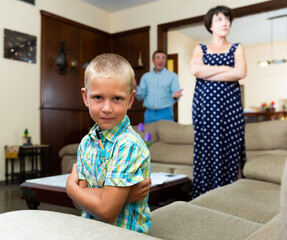 Unhappy small boy sitting at sofa during his parents quarrelling on background at home