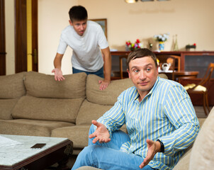 Upset father sitting while quarreling with his teenage son in domestic interior