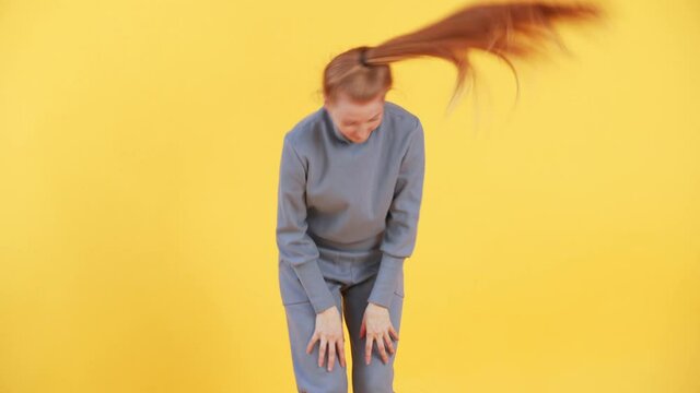 Woman with long ginger hair is twirling her ponytail in a funny way. Yellow background in studio