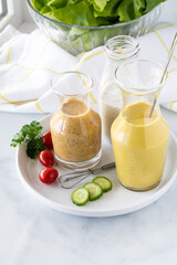 Close up view of salad dressings on a small platter surrounded by salad ingredients.