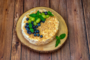Homemade Napoleon cake (Mille-feuille) decorated with grapes, blueberries and mint leaves on a wooden table.