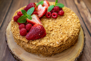 Homemade Napoleon cake (Mille-feuille) decorated with strawberries, raspberries and mint leaves on a wooden table.	