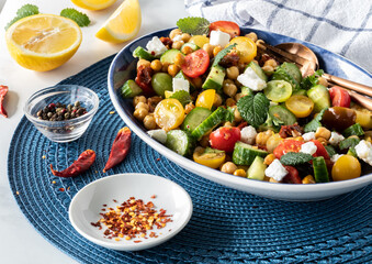 A large serving bowl filled with mediterranean salad and a small dish of chili pepper flakes in front.