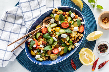 Top down view of a large mediterranean salad surrounded by lemon wedges and spices, ready for...