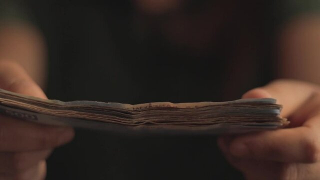 Close up of woman's hands with short nails, giving Mexican five hundred peso bills.