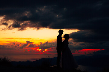 Silhouettes of the bride and groom holding hands at dusk, standing on the seashore