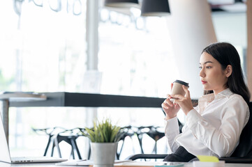 Young businesswoman holding coffee cup sit at her desk, thinking and worrying about work.