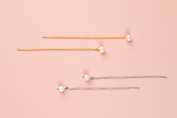 Top view of beautiful luxury gold and silver earrings with pearl on pastel pink surface. Stylish female jewelry