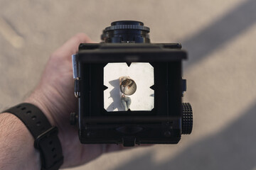 Male hand holding TLR lens of an old medium format camera with a girl being photographed
