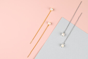 Top view of stylish golden and silver earrings with pearls on pink gray geometric surface. Woman trendy accessories