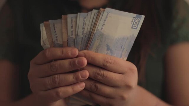 Close up of woman's hands with short nails, counting Mexican five hundred peso bills.