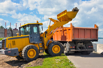the tractor loads the soil into the dump truck. Construction of a new road.