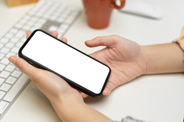Side view of female hands holding smartphone with mock-up screen on computer table