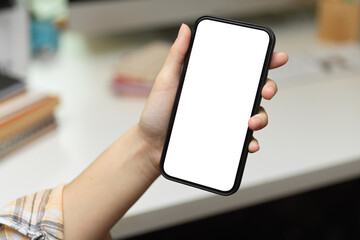 Female hand holding smartphone above workspace and showing mock-up screen to camera