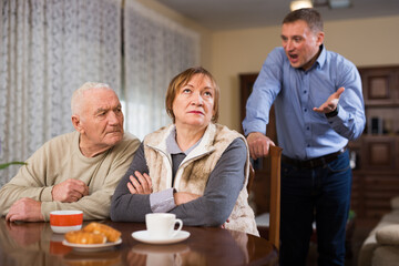 Adult annoyed man scolding his senior parents at home
