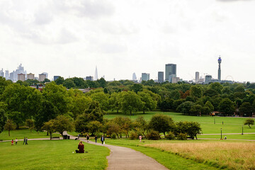 Primrose Hill in London with people sitting on grass. City skyline in misty day.