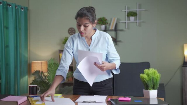 Standing Young busy woman arranging papers on working desk after completion of work - female business woman busy looking documents at home - Concept of wrk from home during coronavirus lockdown.