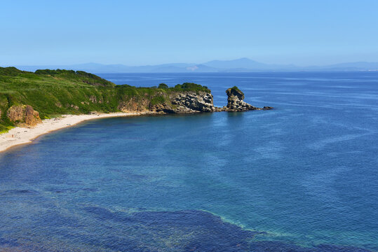 Mountains and seascape with blue sky. Green vegetation in the mountains, sandy beach and amazig sea