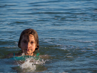 A beautiful girl is bathing in the sea under the rays of the setting sun. A teenage girl enjoys in...