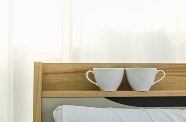 Closeup of two white cup of hot coffe on shelf over bed in bedroom morning.