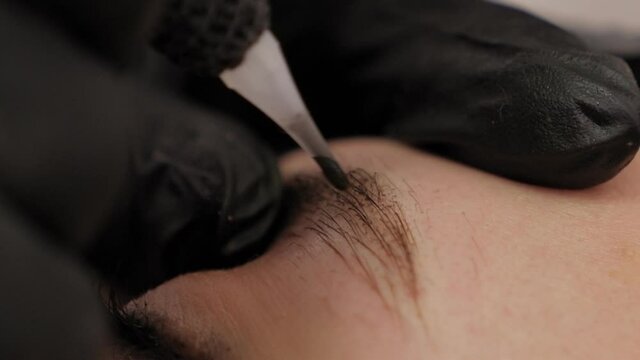 Close-up of a beautician doing permanent eyebrow makeup for a young woman.