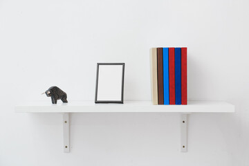 Shelf with books and blank frame on light background