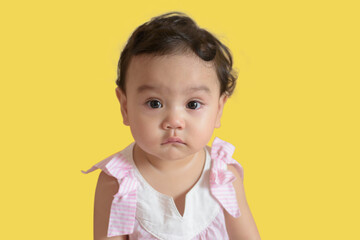 Portrait of a cute little Asian baby girl, look at camera isolated on yellow background, baby expression concept