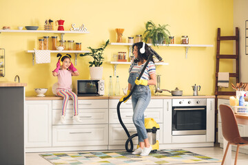 Mother and daughter having fun while hoovering carpet in kitchen