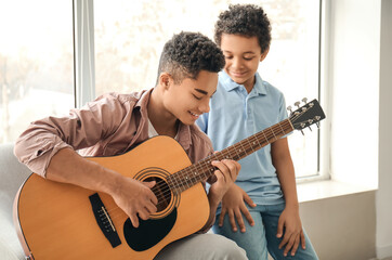 Teenage boy with his little brother playing guitar at home