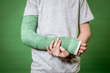 close photo of boy with broken arm with green plaster in front of green background
