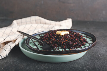 Plate with tasty quinoa and butter on dark background