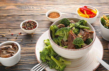 Bowl with tasty beef and broccoli on wooden background