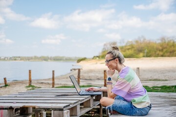 Internet freelance job choice concept: a young woman works on her laptop by the lake. Job outside the office.