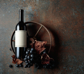 Bottle of red wine with grapes and dried vine leaves on an old rusty background.