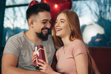 Ginger woman with freckles is receiving a present from her lover during a date at home