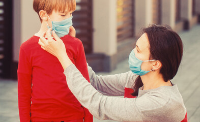 Coronavirus outbreak. Mom with a son in a medical mask. Mother puts her son a face protective mask outdoors