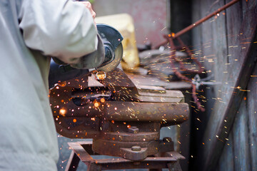 Cutting a metal pipe with a splash of spark. the pipe is clamped in a vice. man's hands hold a grinder. old iron vise, rusty pipe. electric tool, working with metal, cutting with a disc, close-up