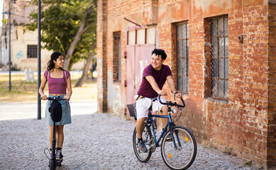 Young couple on the street with bike and electric scooter.