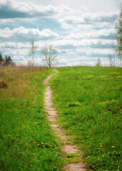 a path going up the slope to the skyline, a footpath going to the horizon along the field with green grass, blue cloudy sky 