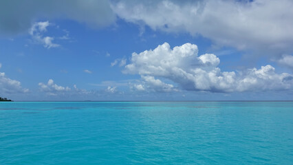 The aquamarine ocean is calm. There are picturesque cumulus clouds in the azure sky. Summer sunny day. Maldives idyll