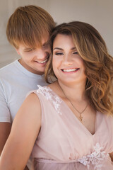 Young pretty pregnant woman hugging and smiling with handsome husband in studio