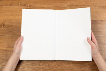 Obraz premium Woman holding brochure with blank cover on wooden background, top view. Mock up for design