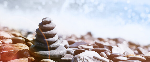 Banner. Stone pebble tower balancing on the beach with sparkling sea waters splash bokeh. Copy space. Balance and mindfulness. Summer travel and vacation. rainbow reflection